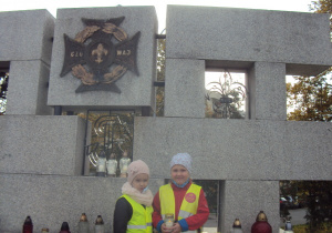 Nadia i Zuzia stawiają znicze pod pomnikiem Harcerzy